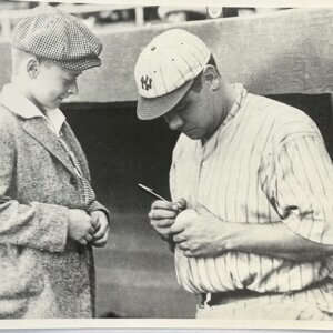Babe Ruth signing a baseball for a young fan in classic 1920s Yankees uniform