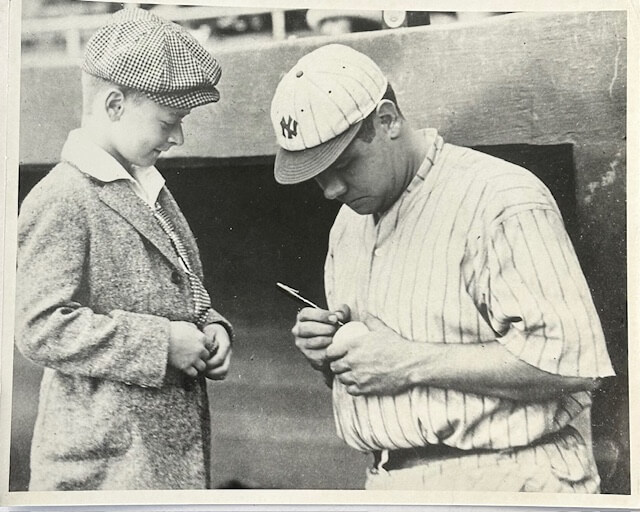 Babe Ruth signing a baseball for a young fan in classic 1920s Yankees uniform