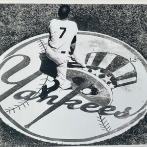 Mickey Mantle standing in the on‑deck circle with Yankees logo and number 7 on his back.