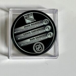Clear display case holding a New York Rangers commemorative puck featuring retired numbers for Mike Richter, Eddie Giacomin, and Rod Gilbert.